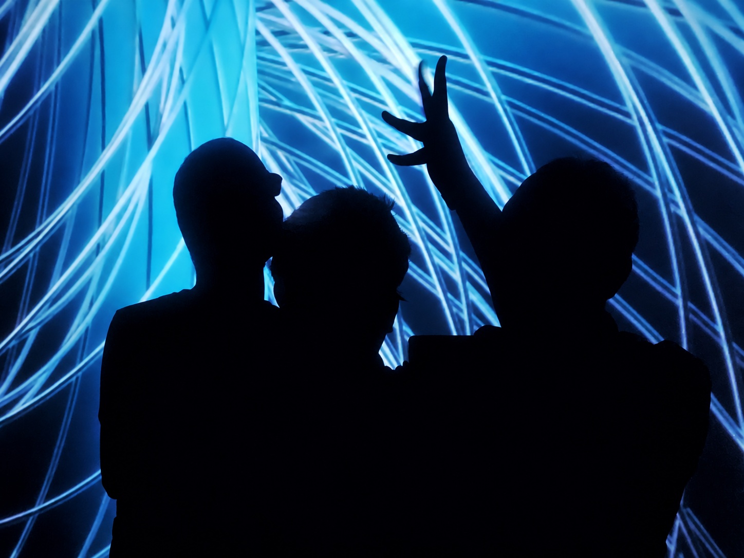 Three silhouetted figures against an electric blue light installation